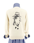 Ivory sweater with a Paddington Bear design in back, layered over a blue striped shirt