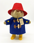 Plush Paddington Bear wearing a red hat, blue duffle coat, and yellow boots, with a tag reading, "Please look after this BEAR. Thank you.