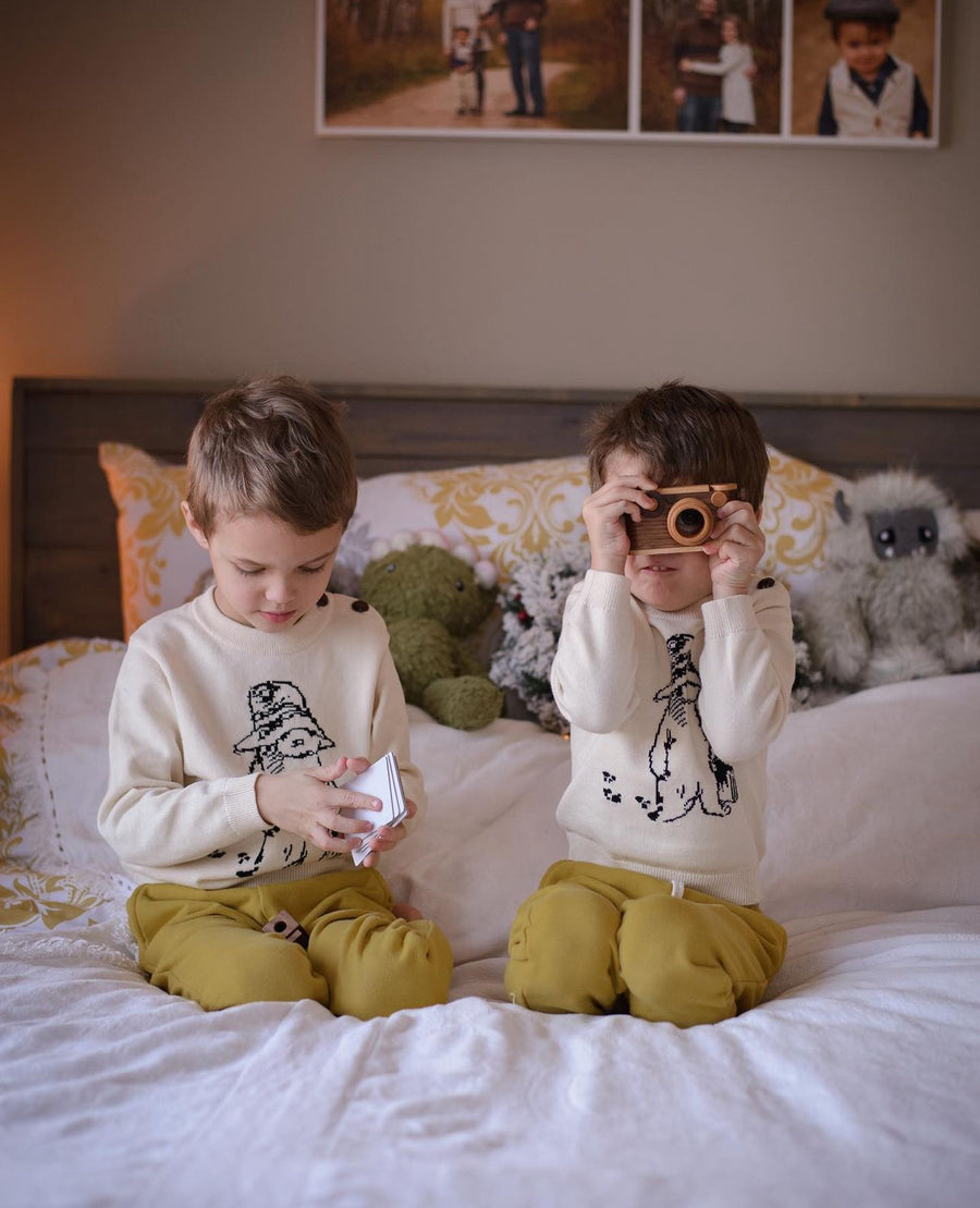 Two kids wearing Paddington Bear sweaters on a bed.