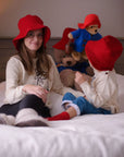 Mother and child wearing red hats and Paddington bear sweaters, playing with soft toys