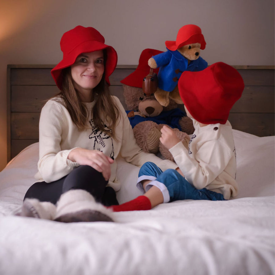 Mother and child wearing red hats and Paddington bear sweaters, playing with soft toys