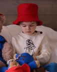 child wearing a red hat and a Paddington bear sweater, playing with a stuffed bear