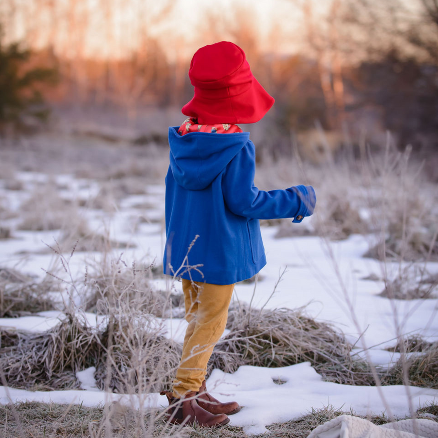 Child in red hat and blue coat walking in snowy field