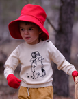 Child in red hat and gloves wearing a sweater with a bear design