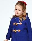 Young girl in a blue duffle coat with toggle closures, wearing a red bow