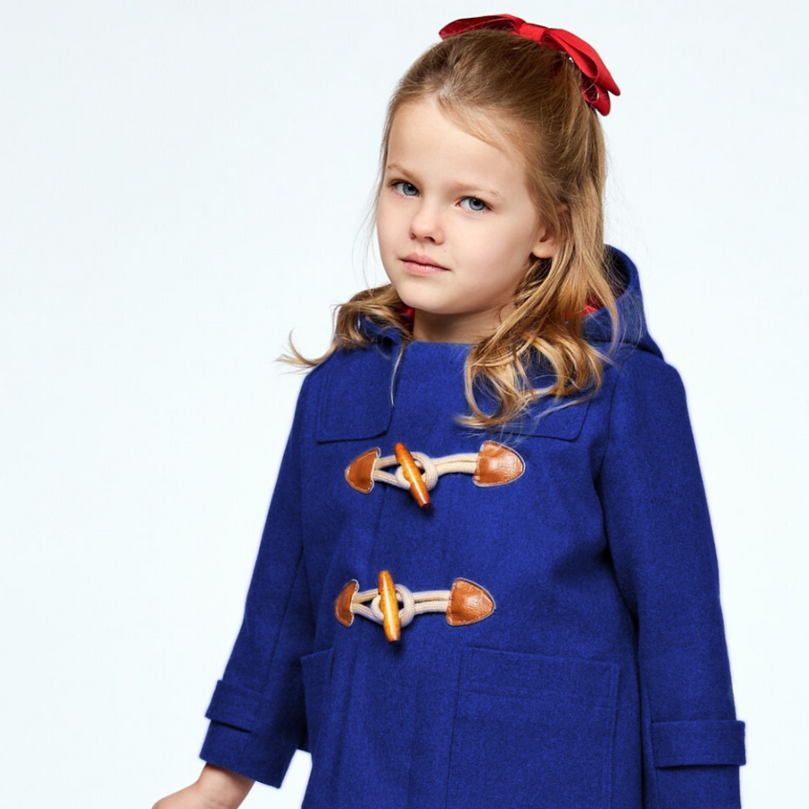 Young girl in a blue duffle coat with toggle closures, wearing a red bow