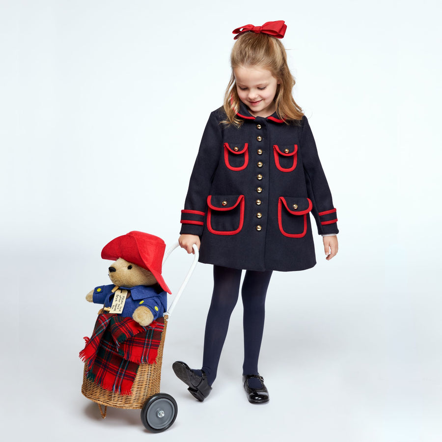 Girl in a navy coat pulling a Paddington Bear toy