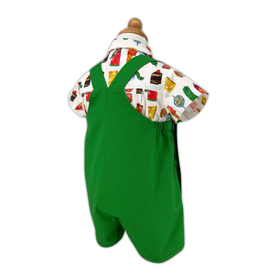 back view of a green romper with crossed straps displayed on a mannequin, paired with a short-sleeved shirt featuring a colorful food-themed print