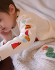 Child wearing a beige-colored sweater with embroidered food illustrations on the right sleeve,