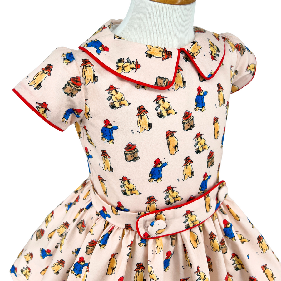 Close-up of a Paddington Bear print dress with red piping and a belt.