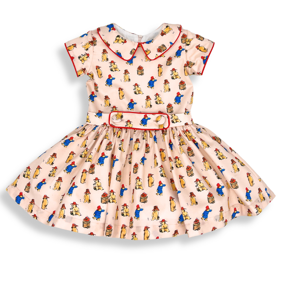 Pink vintage-style dress with Paddington Bear print, red piping, and a matching belt