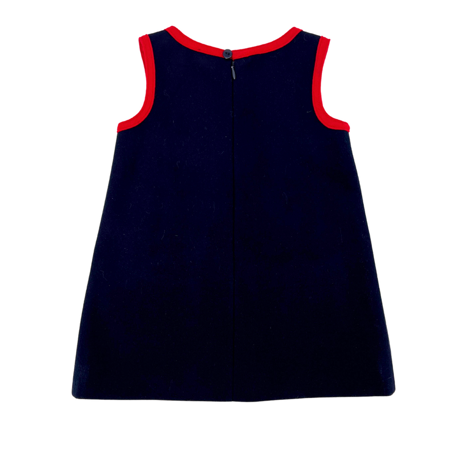 Back view of the Little Goodall Girls Pocket Paddington Bow Dress in dark blue wool with red trim. A-line silhouette, sleeveless, with button closure.