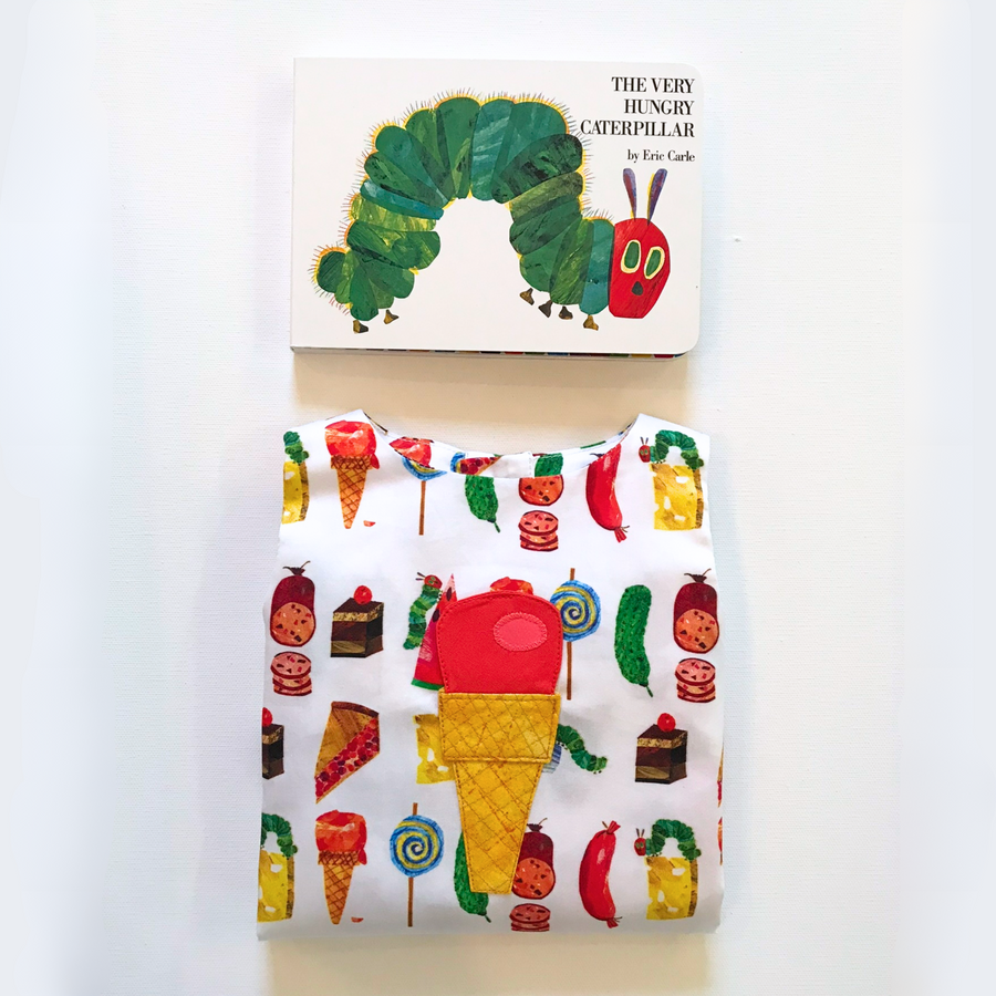 Folded Hungry Caterpillar romper for boys and girls with colorful food prints, made from 100% cotton, displayed with the matching board book 