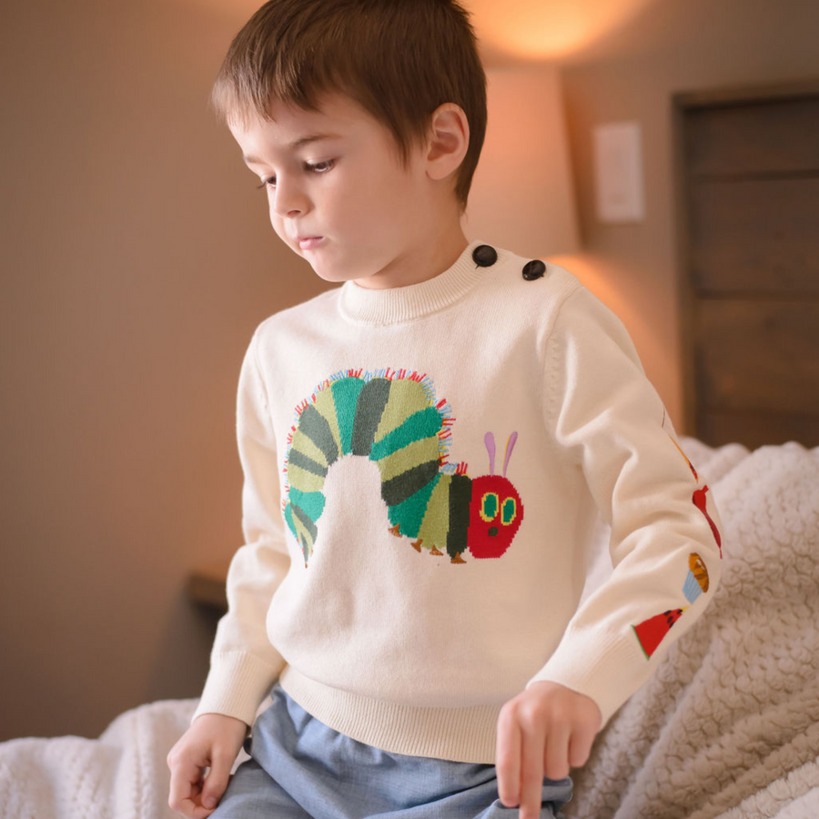 A cozy beige knit Hungry Caterpillar sweater worn by a child, featuring a vibrant caterpillar and embroidered food illustrations.