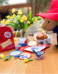 Paddington Bear with the Little Goodall Paddington Tin Tea Set, featuring a teapot, cups, saucers, and a red travel case, perfect for tea parties