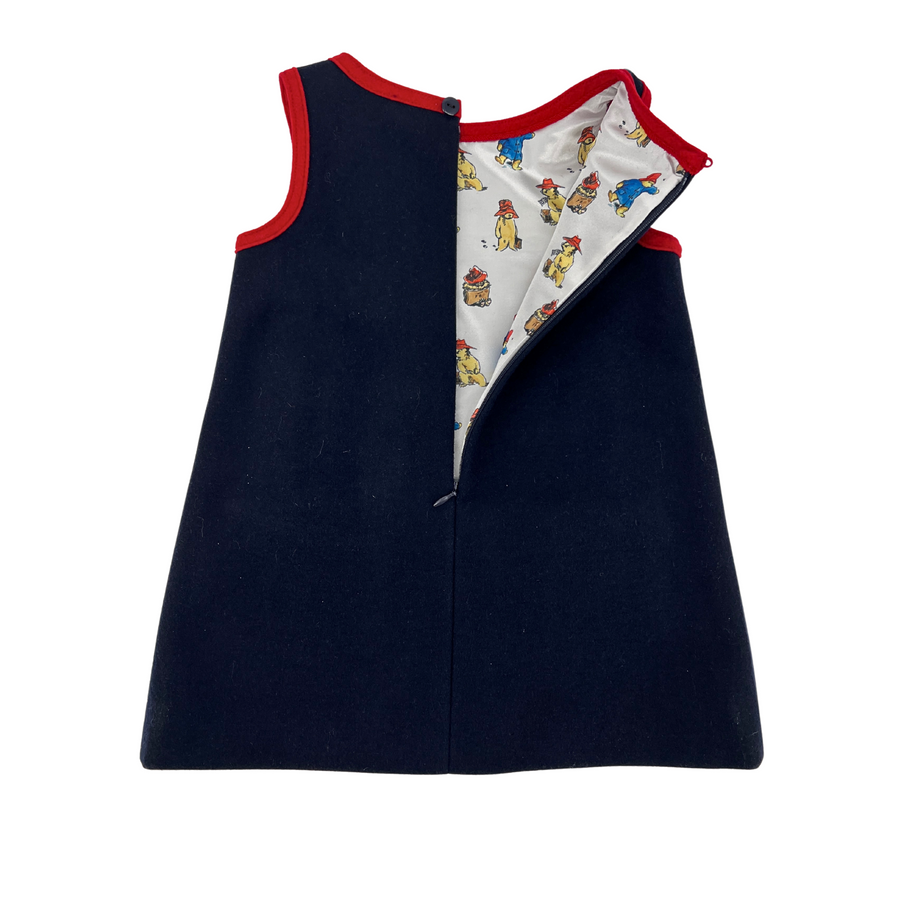 Back view of a girls' wool dress with red trim, with back zipper opened to reveal a satin lining with a Paddington bear fabric print.