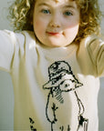 Child wearing an ivory sweater with a black line drawing of a character