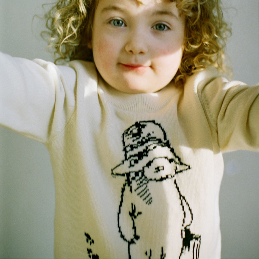 Child wearing an ivory sweater with a black line drawing of a character