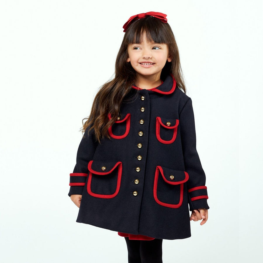 Smiling girl wearing a navy coat with red trim and gold buttons